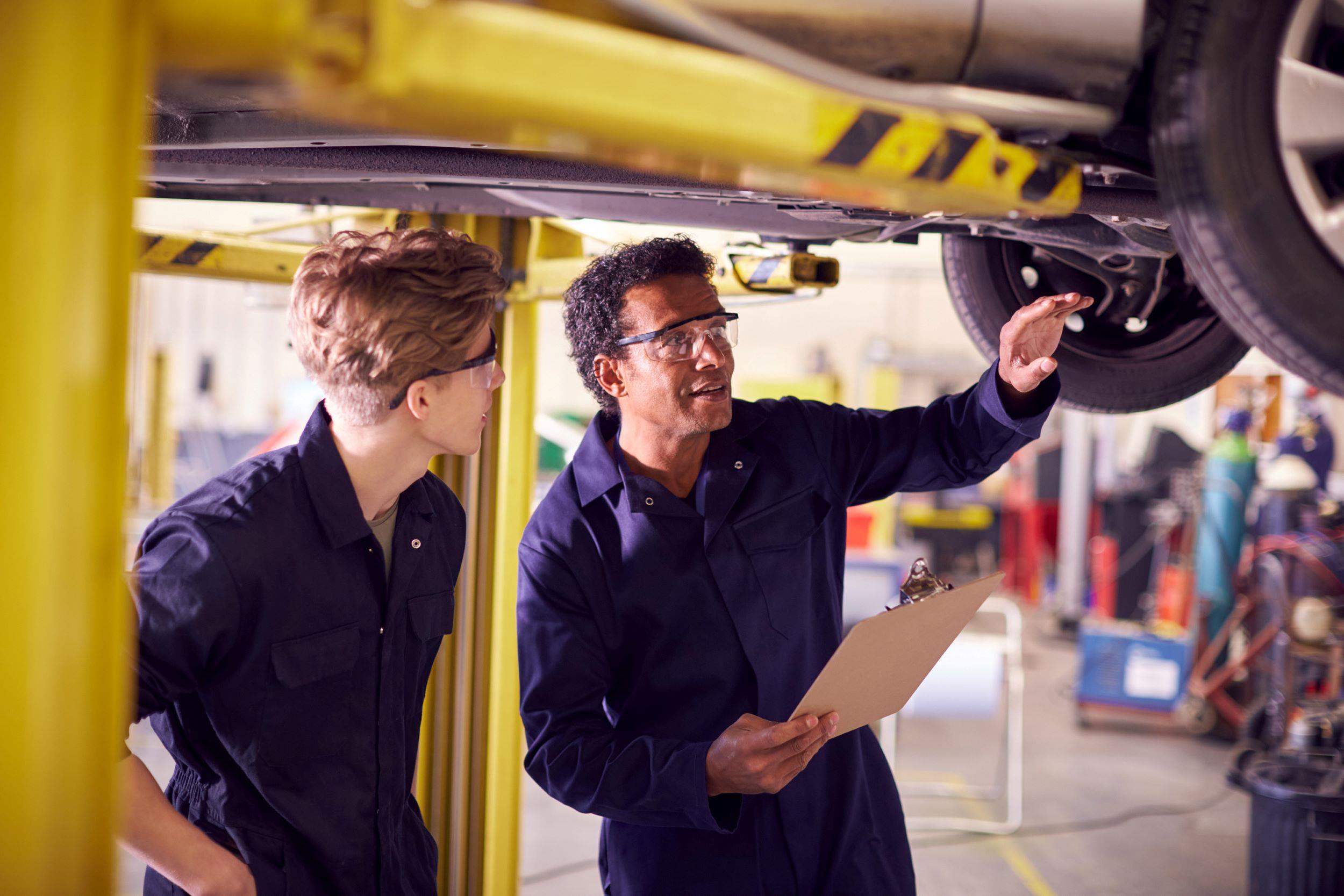 A mechanic showing an apprentice underneath a car