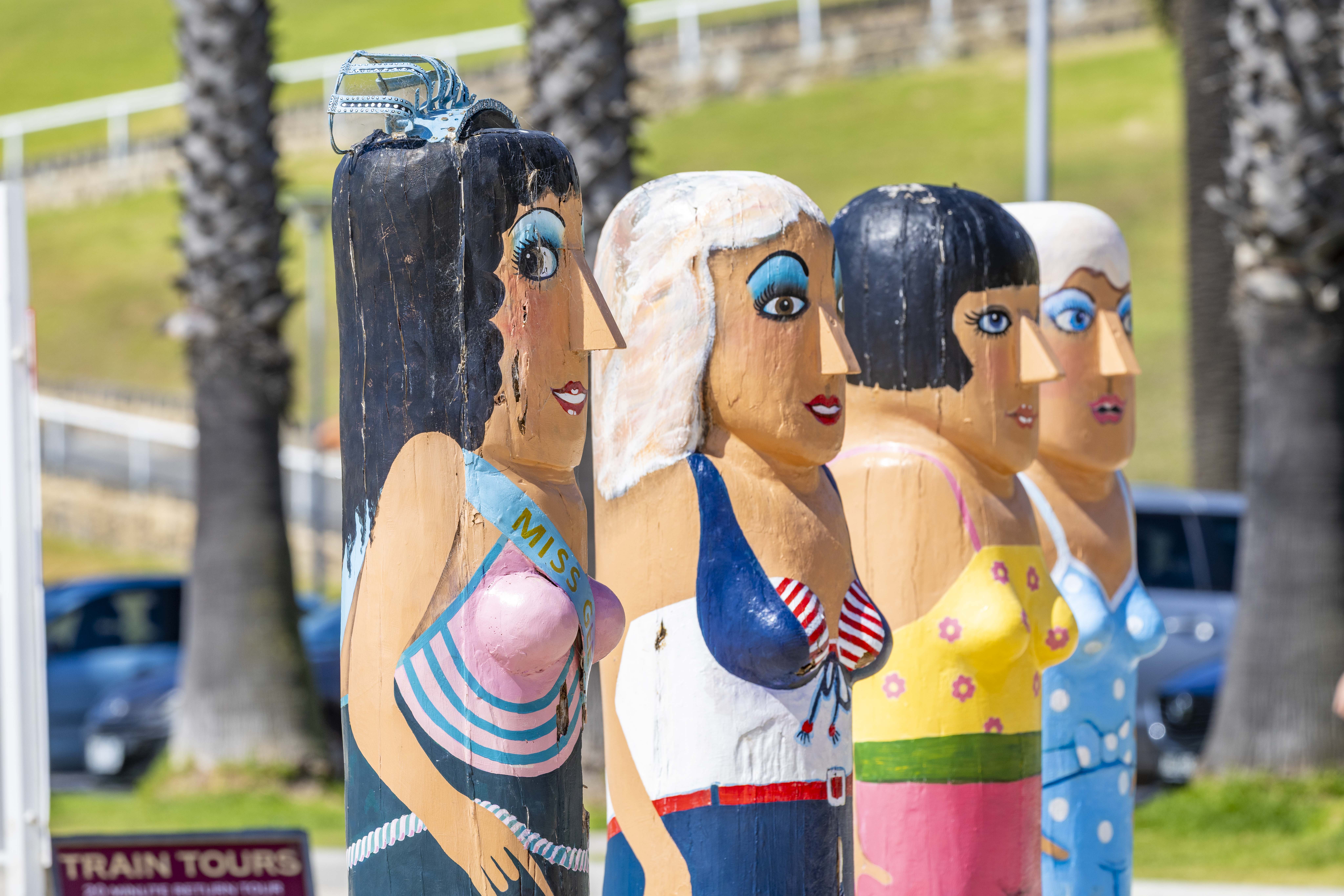 Painted bollards of four beauty contestants all wearing bathing suits and make-up.