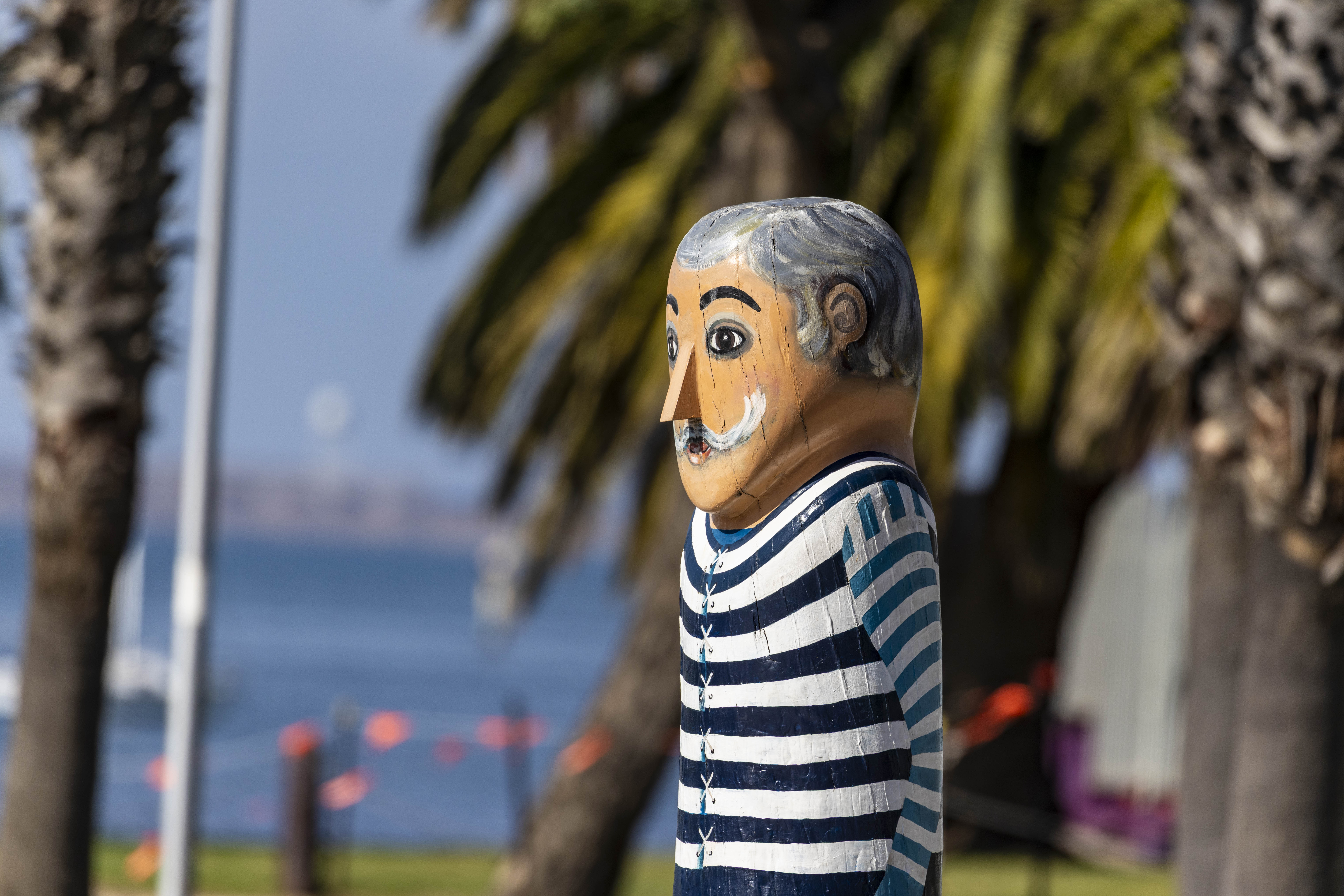 Painted bollard of an old Geelong football player with grey hair and large mustache. He is holding a red football.