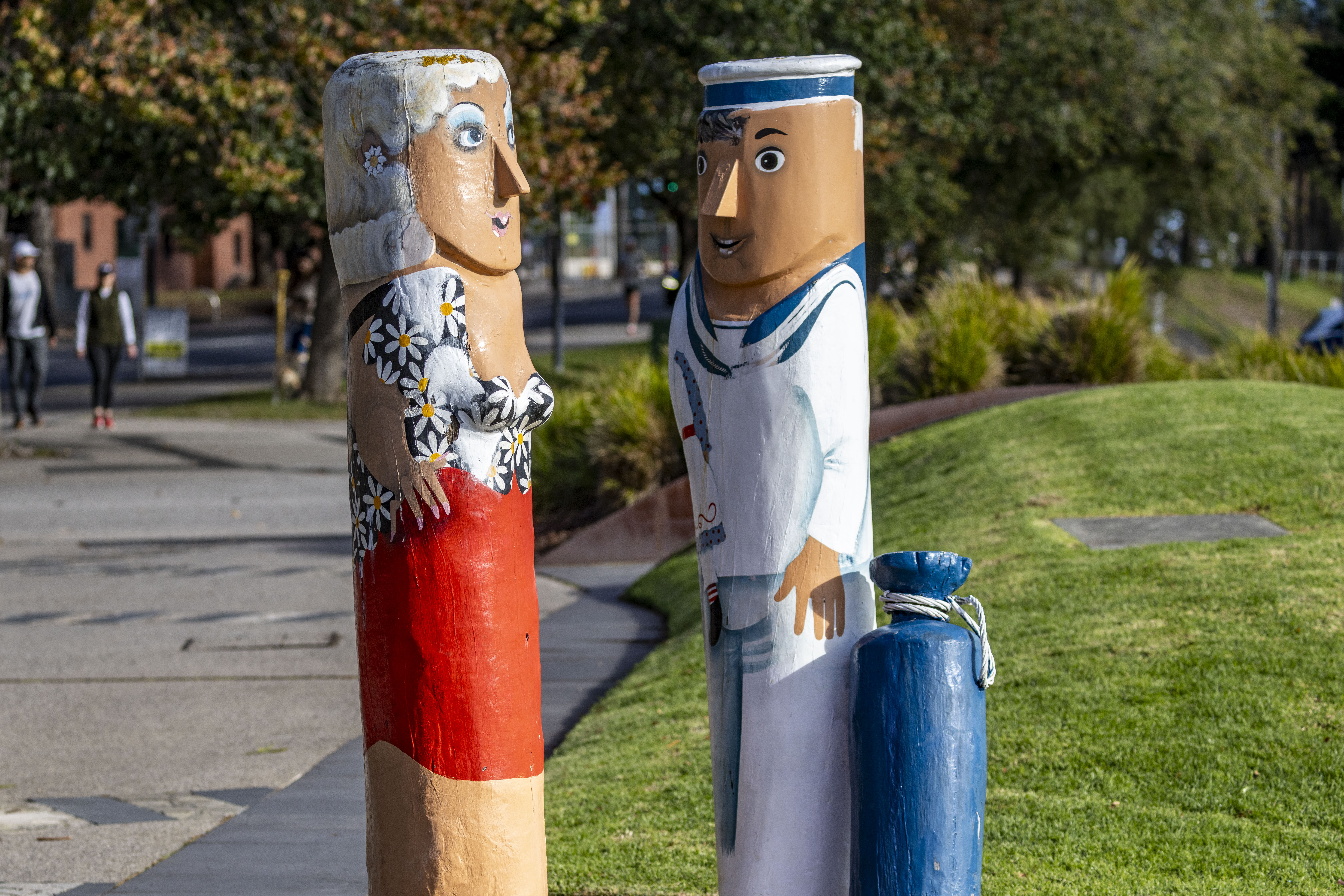 Painted bollards of a woman and a sailor. The sailor has a blue bag indicating he is on shore leave.