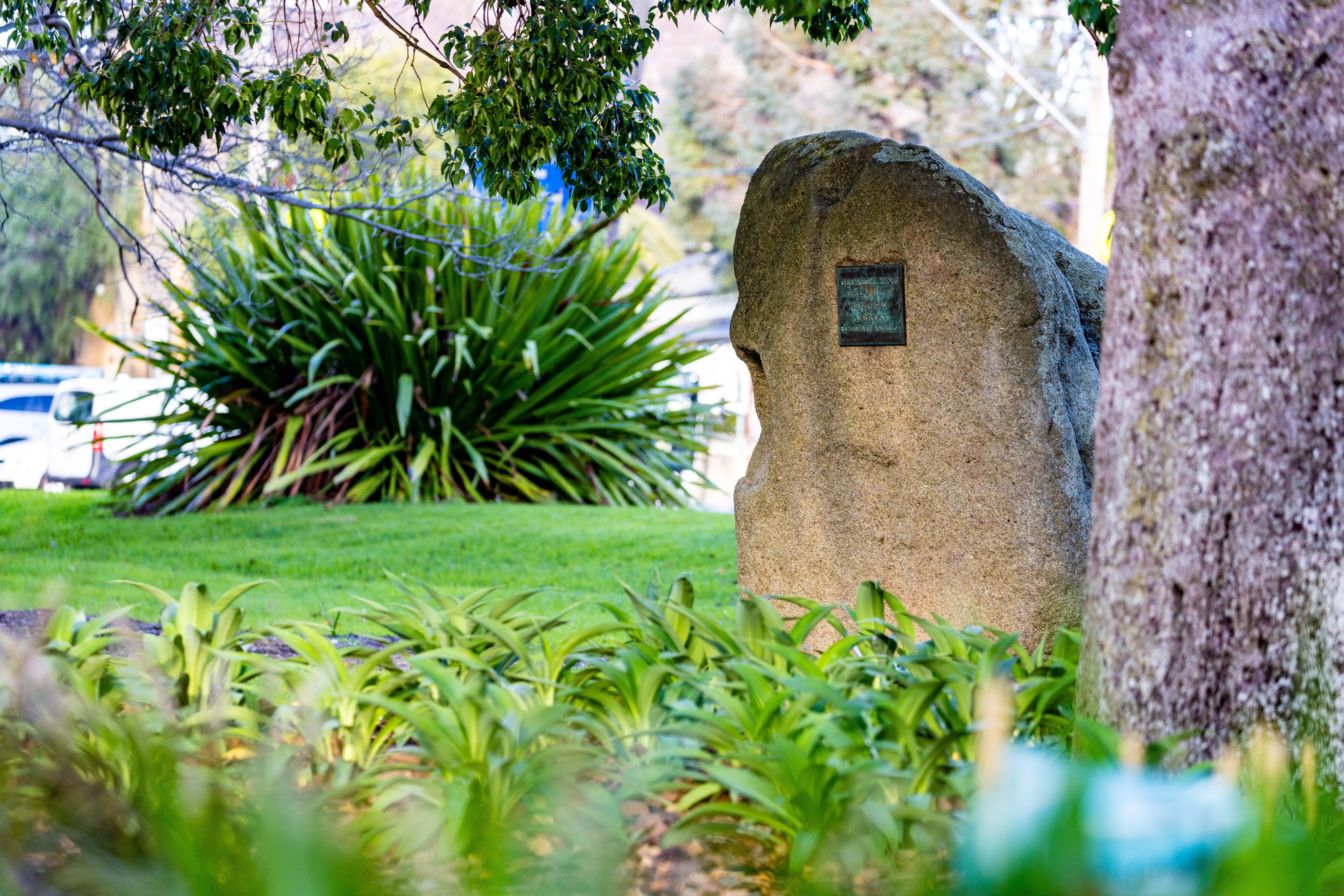 Large boulder with bronze plaque sitting in green park.