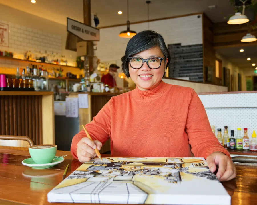 Image of female wearing orange top and glasses, drawing in a cafe