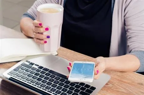 Lady holding mobile phone sitting in front of computer