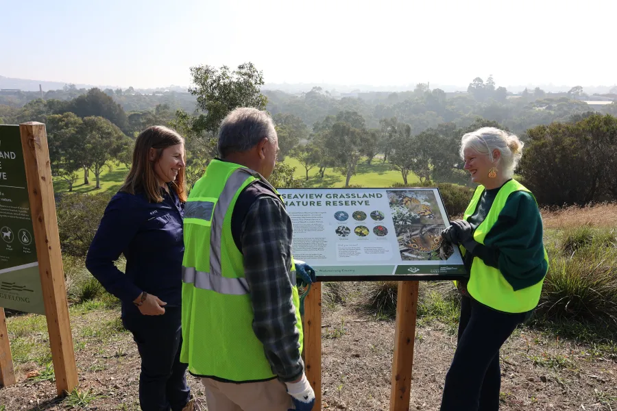 Environment and Biodiversity officer Kate Constance stands with Geelong Field Naturalist Club member Rod Lowther and Cr Elise Wilkinson around a Seaview Grassland Nature Reserve information sign.