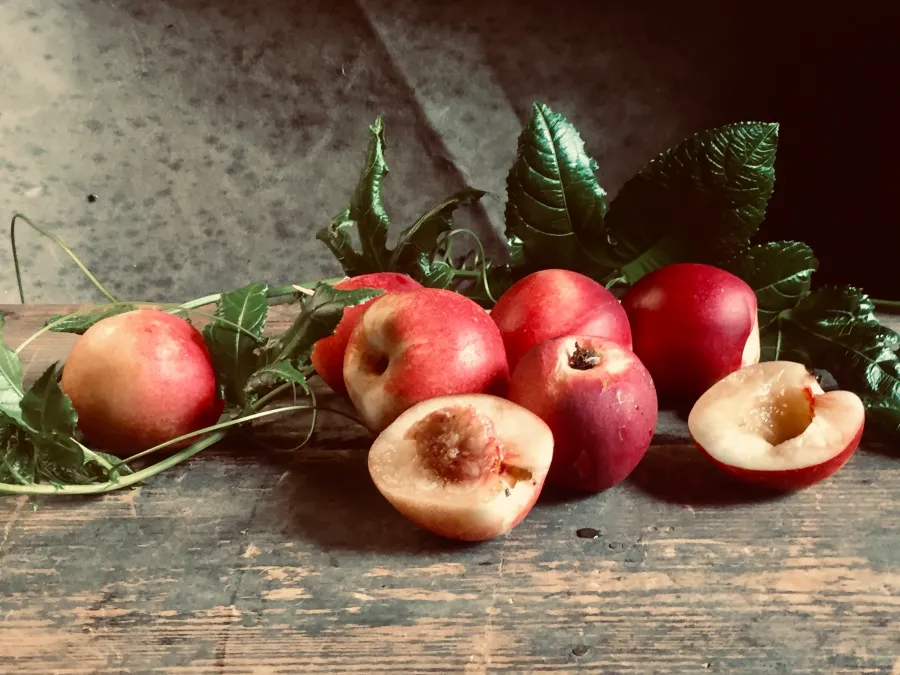 Fresh whole and halved red nectarines with green foliage displayed on a rustic wood surface