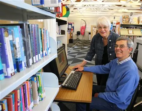 Man sitting at computer with woman standing providing guidance