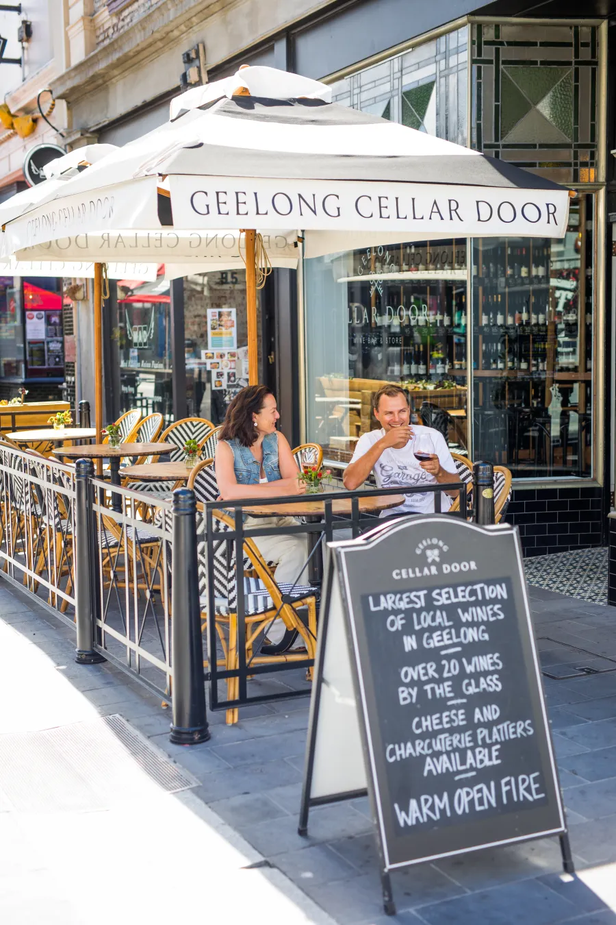 Example of Outdoor Dining with two people enjoying dining outside Geelong Cellar Door, there is a A-Frame sign in the foreground
