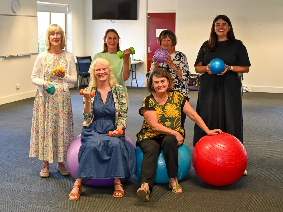 Women standing and sitting holding various exercise equipment.