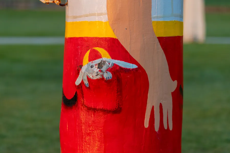 Grey rabbit with a red and yellow swim cap at the base of a bollard