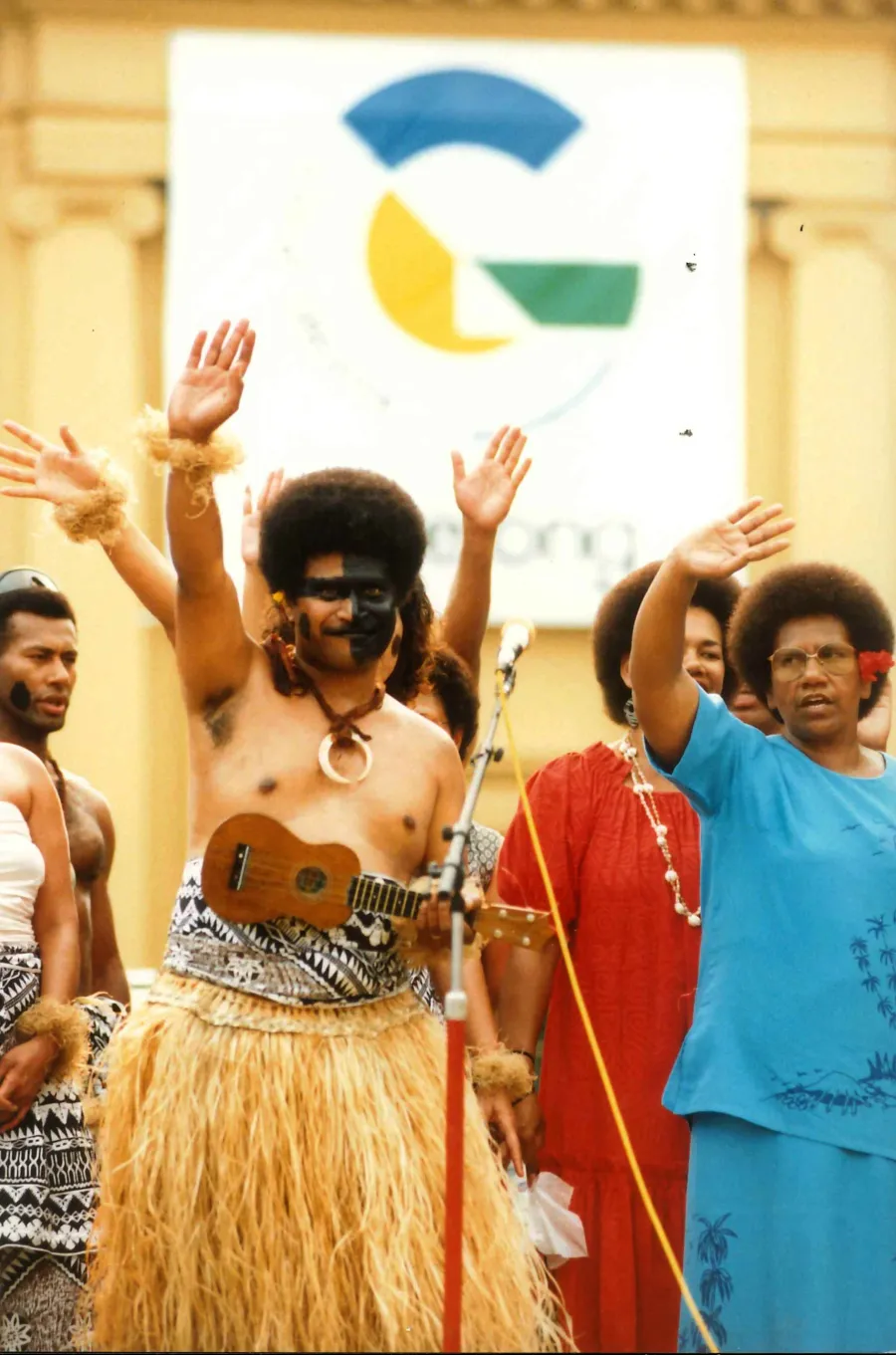 Fijian community members in cultural dress with their hands up in the air