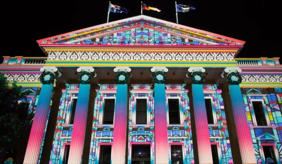 Geelong City Hall illuminated at night with colourful projected light displays in pink, blue, green and gold. The heritage building’s columns, windows and decorative façade are highlighted by the vibrant projections against a dark sky.
