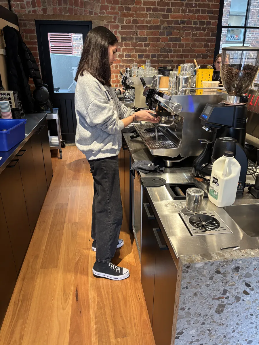 Espresso Basic Coffee Course person wearing grey jumper and black pants at a coffee machine learning to make a coffee