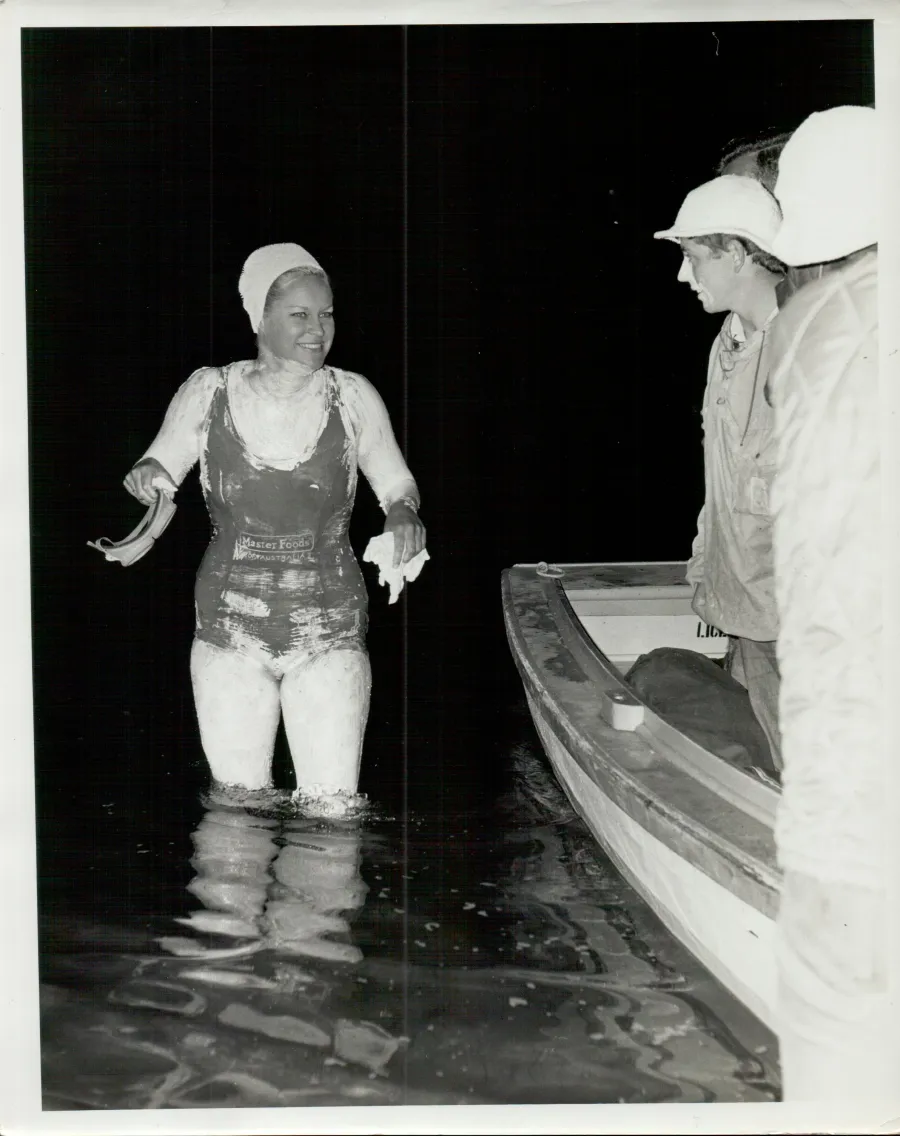 Woman standing in water next to people in boat