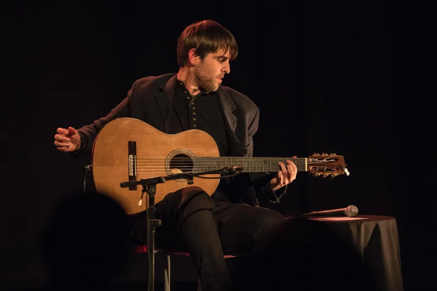 Pau Figueres playing acoustic guitar on stage.