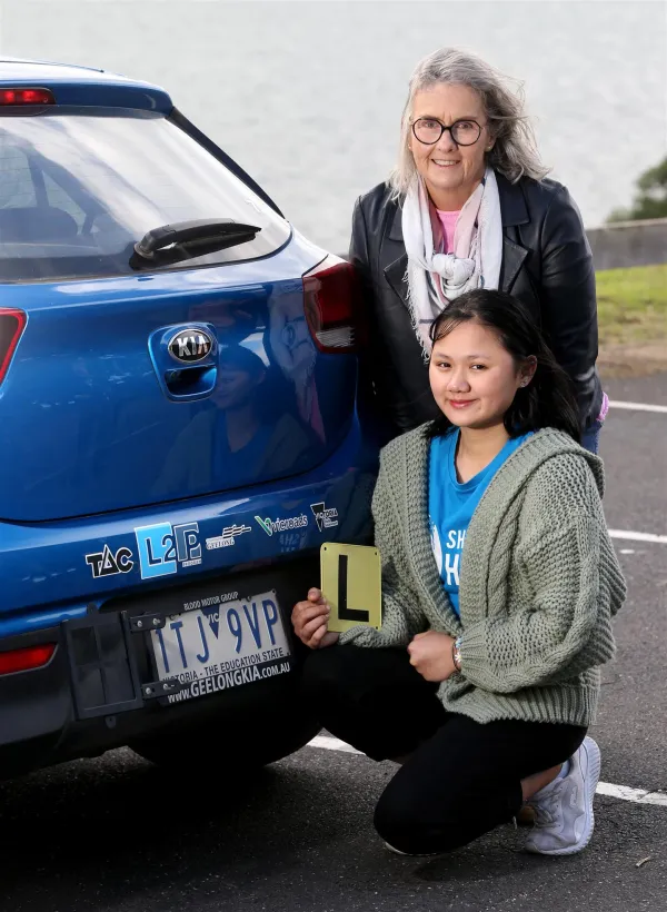 person holding L plates in front of a car with mentor standing behind them