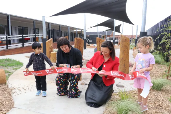 Two women cut a ribbon being held by two young children in a playground