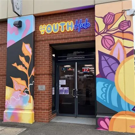 Front of The Nest Youth Hub with neon signage and floral mural on pillars either side of entrance