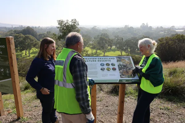 Environment and Biodiversity officer Kate Constance stands with Geelong Field Naturalist Club member Rod Lowther and Cr Elise Wilkinson around a Seaview Grassland Nature Reserve information sign.