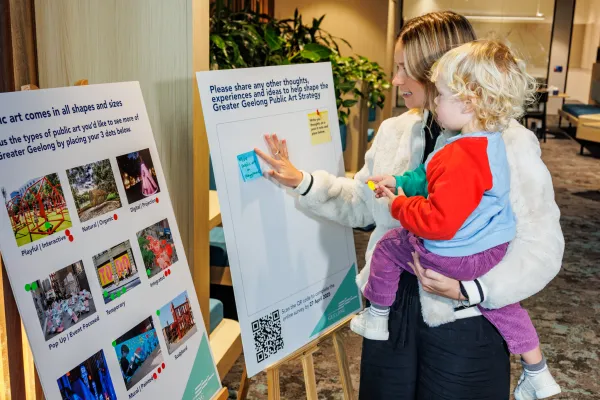 A community member is holding a small child while providing feedback at a community consultation for the Greater Geelong Public Art Strategy.