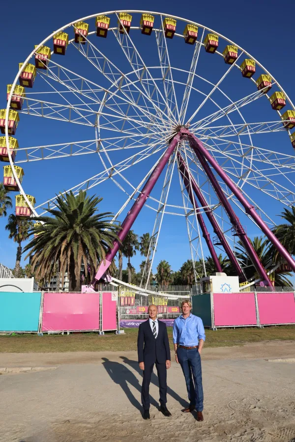 Greater Geelong Mayor Stretch Kontelj is standing with Giant Sky Wheel and café and Waterfront Train operator Brandon Verfurth in front of the Giant Sky Wheel at the waterfront. 