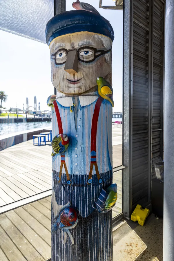 Bird Man Painted bollard of local man with striped shirt, glasses, red suspenders and pants. His hat and clothes are covered in his colourful pet birds.