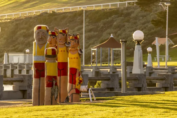 Eastern Beach Lifesavers Five painted bollards dressed in traditional red and yellow lifesaving outfits. They are standing in a row and holding a rope above their heads.