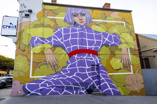 Large scale mural of a woman in a purple jumpsuit on a yellow background painted on the side of a building