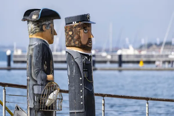 Sea and Steam Captain Two bollards of a steamboat captain and a sail captain dressed in blue suits and caps. One is holding a cage with a cockatoo inside.