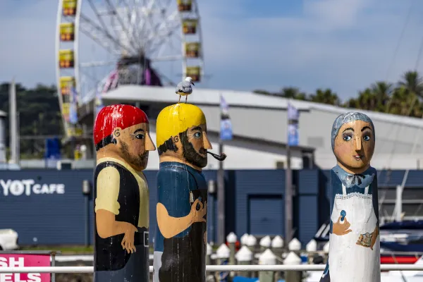 Scallop Fishermen and Woman Three painted bollards of an old woman wearing a white apron and holding a scallop with two bearded fishermen. One has a red hat and the other has a yellow hat.