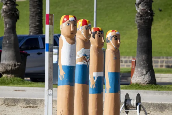 Town Baths Swimmers Club Four painted bollards of swimmers wearing blue shirts and white shirts and standing next to a rope reel.
