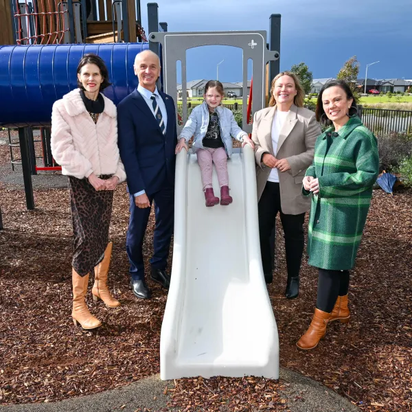 Adults standing around a child on a slide.