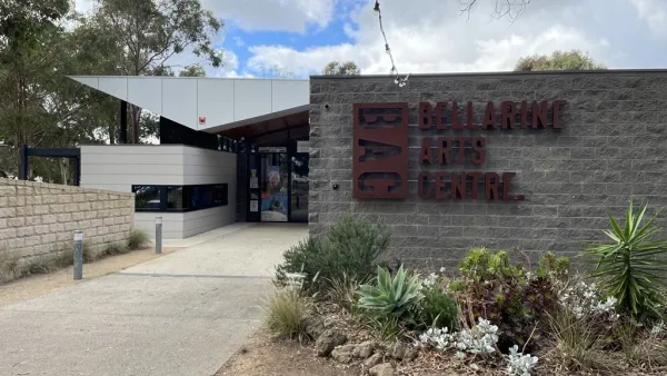 Exterior image of grey building with green garden in front and brown text on the front wall