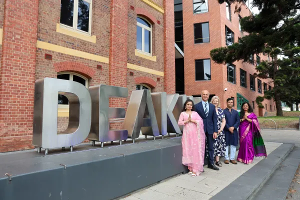 Five people standing in front of Deakin signage, some are wearing traditional cultural dress.