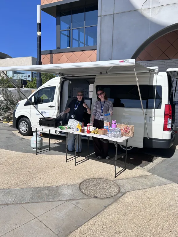 white van with two people standing under the annex with a table and bbq