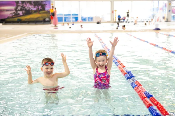 Two children in the pool, with their arms in the air