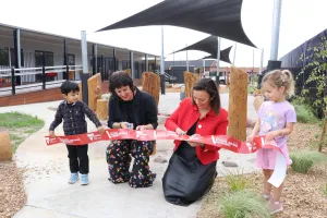 Two women cut a ribbon being held by two young children in a playground