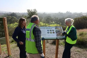 Environment and Biodiversity officer Kate Constance with Geelong Field Naturalist Club member Rod Lowther and Cr Elise Wilkinson at Seaview Grassland Nature Reserve. Environment and Biodiversity officer Kate Constance stands with Geelong Field Naturalist Club member Rod Lowther and Cr Elise Wilkinson around a Seaview Grassland Nature Reserve information sign.