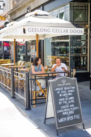 Example of Outdoor Dining with two people enjoying dining outside Geelong Cellar Door, there is a A-Frame sign in the foreground