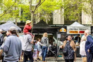 Man carries child on shoulders through market crowds past stalls