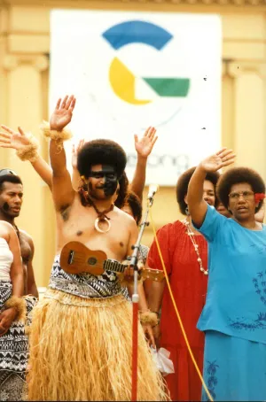 Fijian community members in cultural dress with their hands up in the air