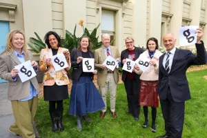 Seven people holding pieces of paper with the letter 'G' and smiling