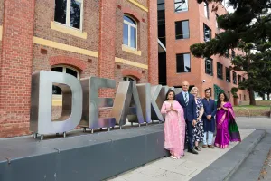 Five people standing in front of Deakin signage, some are wearing traditional cultural dress.