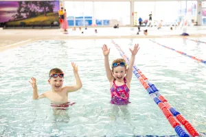 Two children in the pool, with their arms in the air