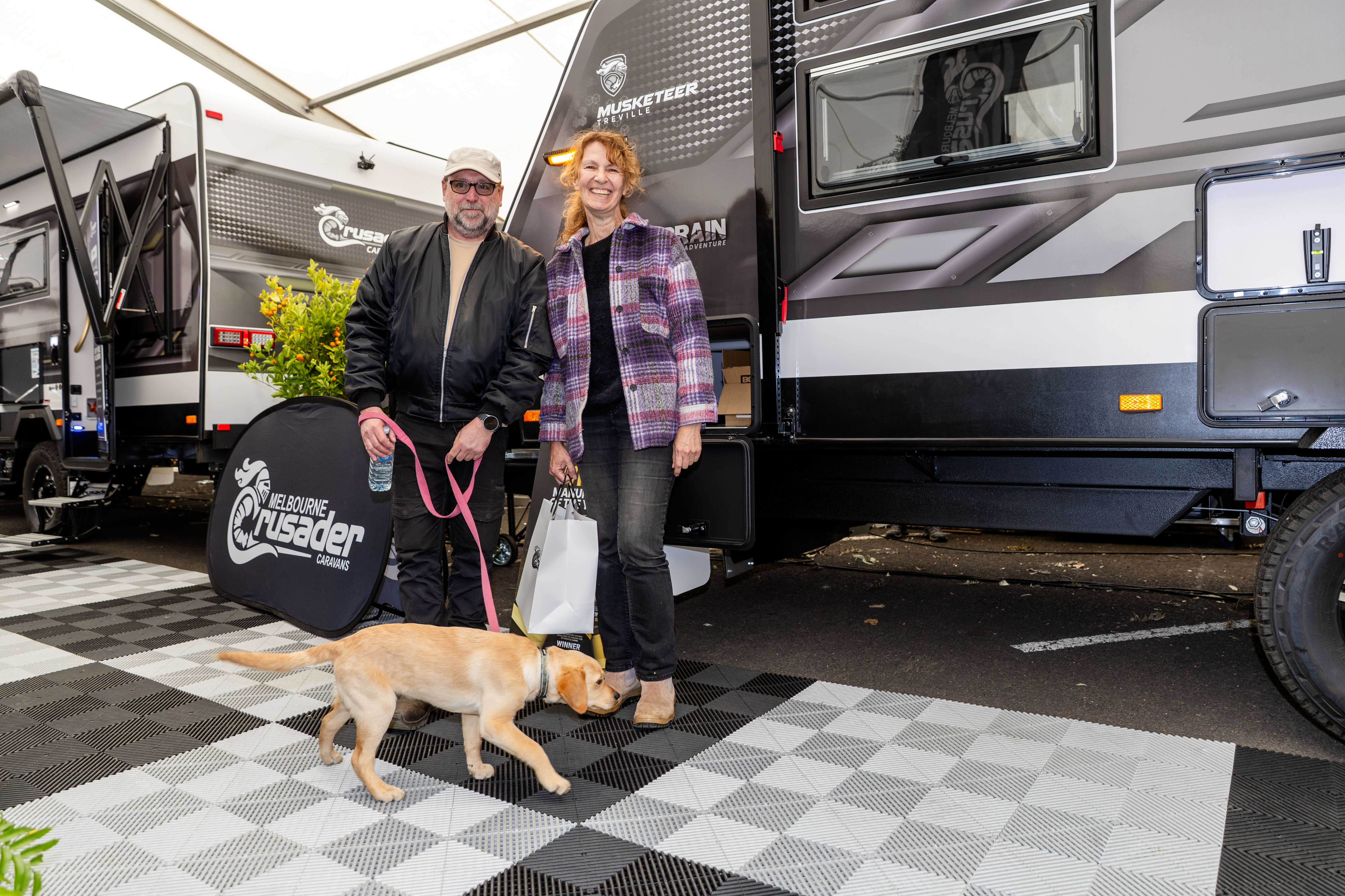 Two people and a dog in front of a caravan